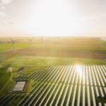 The sun shines over a solar and wind field.